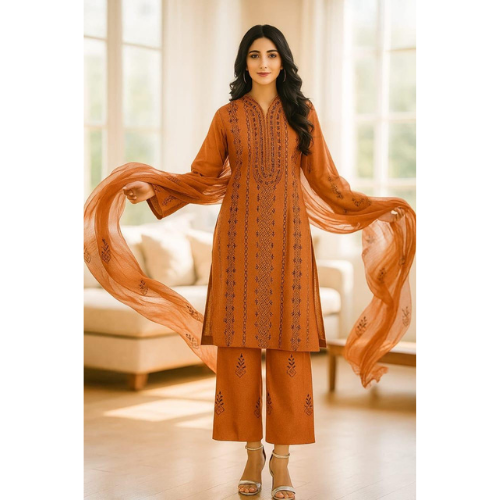 Woman wearing an orange embroidered outfit with a sheer dupatta in a bright room.